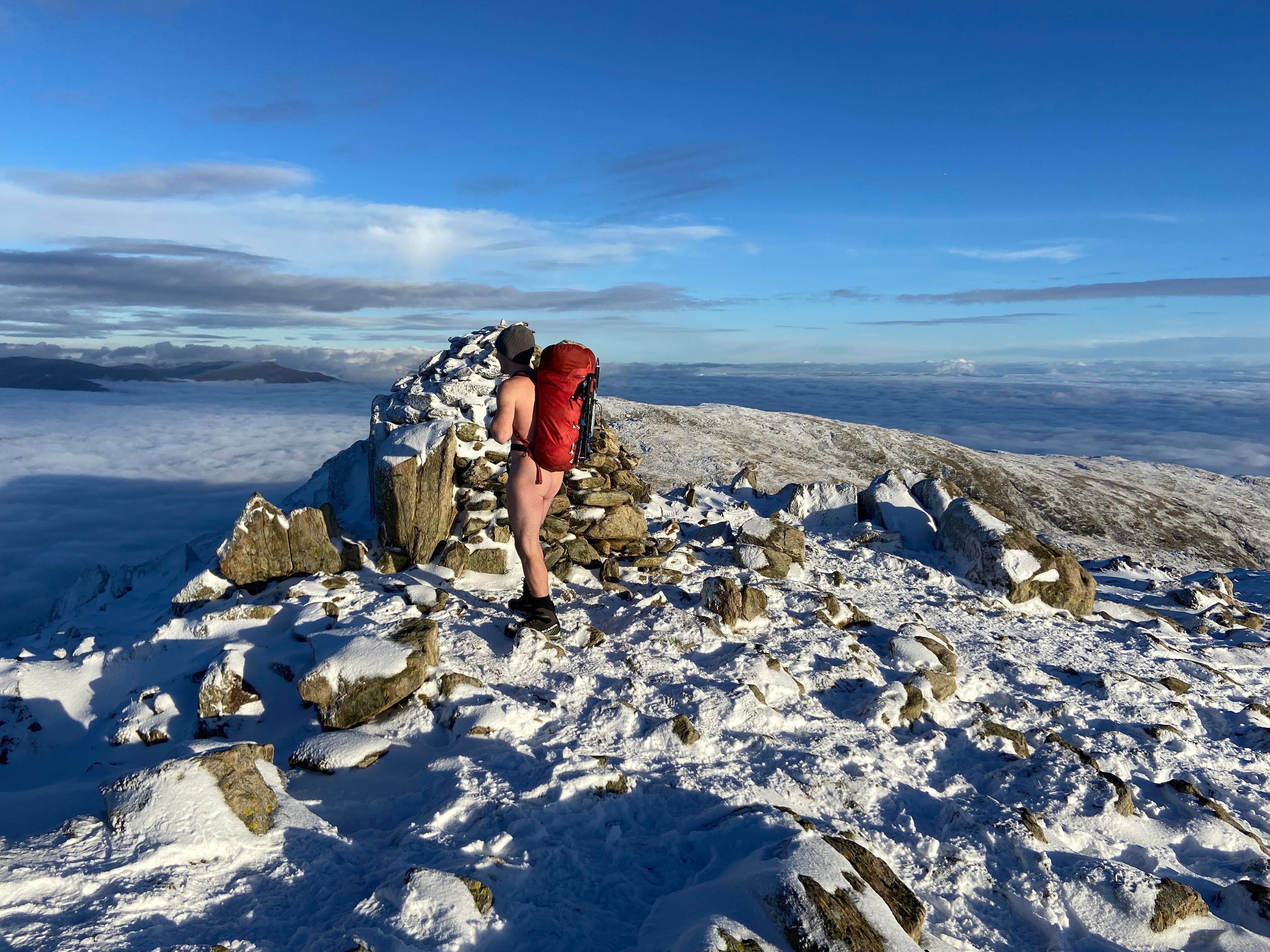 Neil naked on a snowy mountain, looking down on a sky blanketed by clouds
